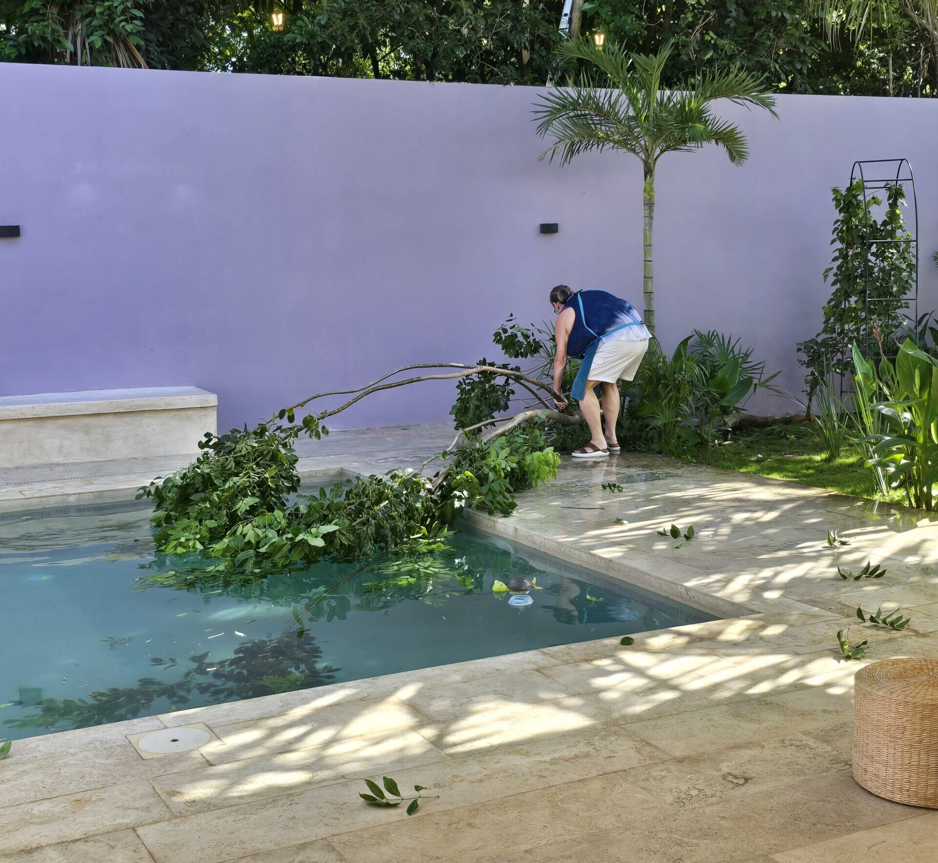 Heather bent over with her apron on, pulling a very large tree branch off the plants and out of the pool